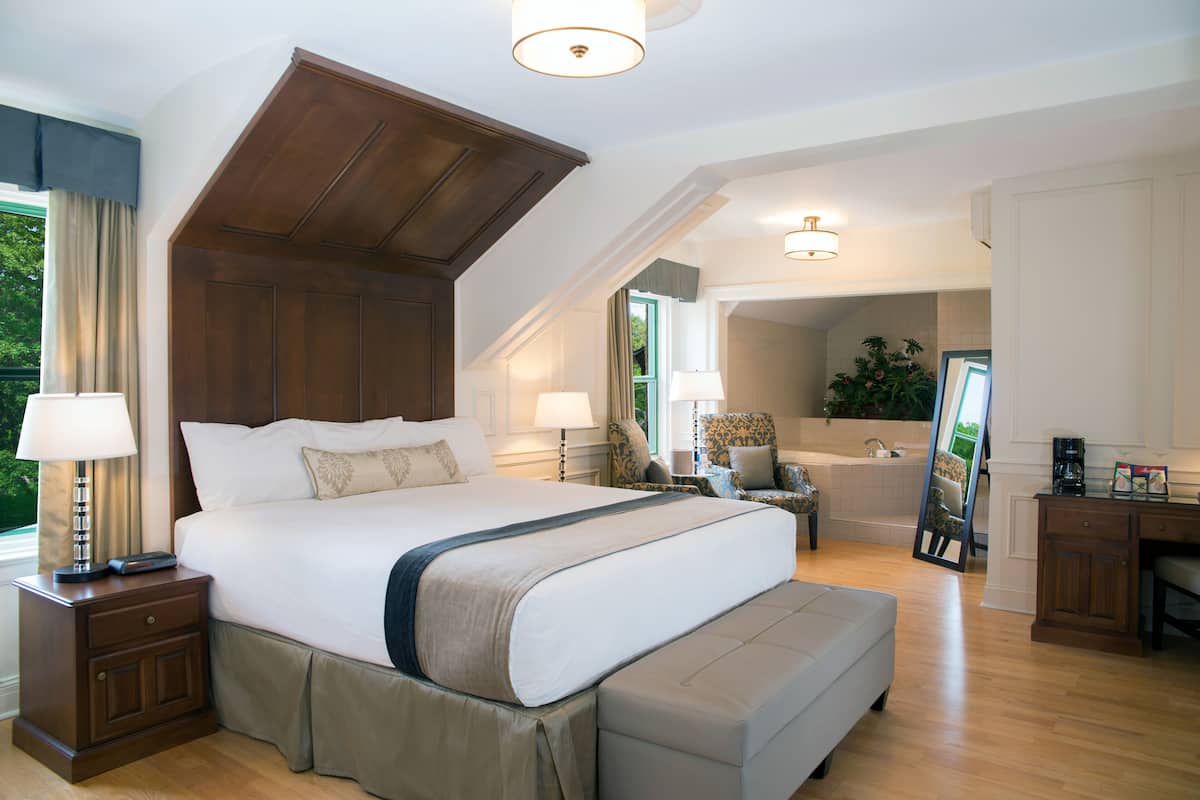 A spacious bedroom with a large bed, a sitting area with a chair, a desk, and a view of a bathroom.