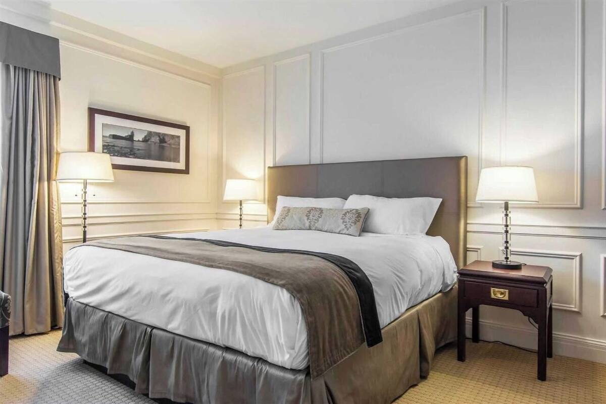 A hotel room with a large bed, two bedside tables with lamps, a framed picture on the wall, and a window with curtains.
