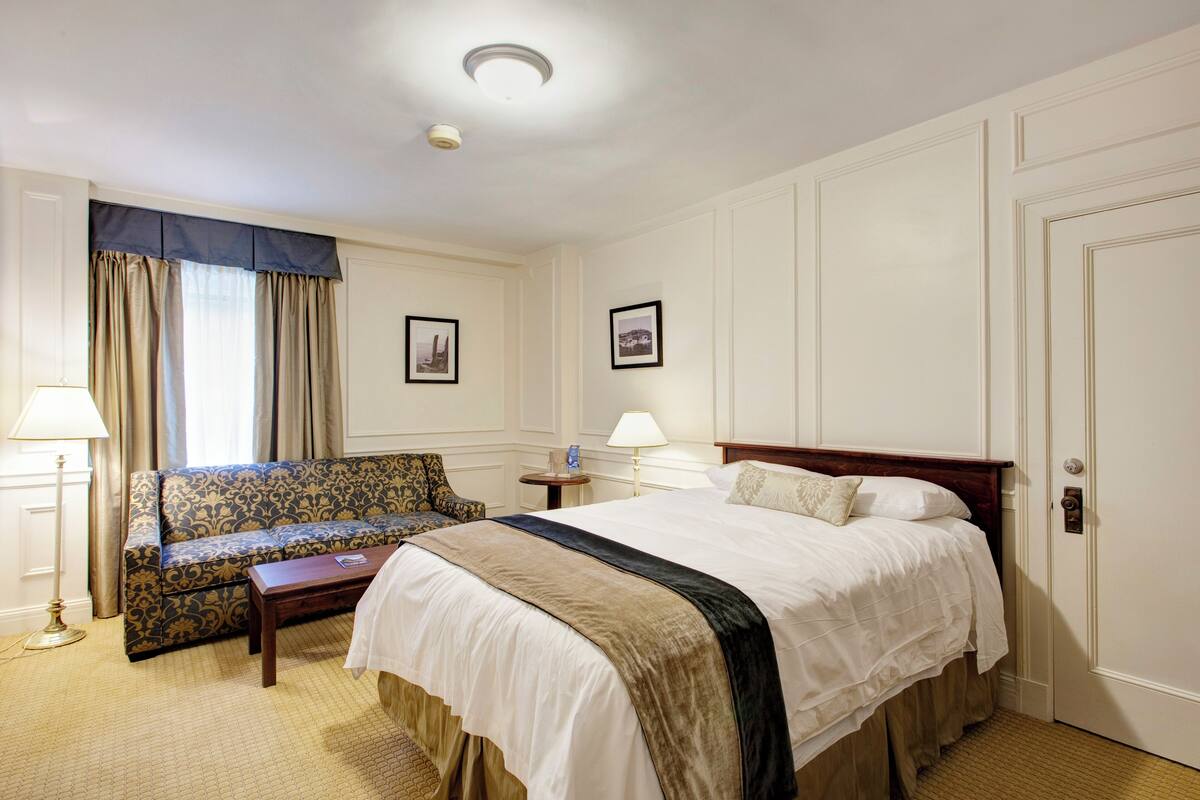 A hotel room with a bed, a sofa, a small table, and a lamp.