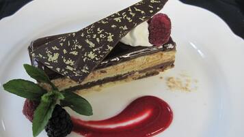 A slice of layered cake with chocolate and raspberry garnish on a white plate.