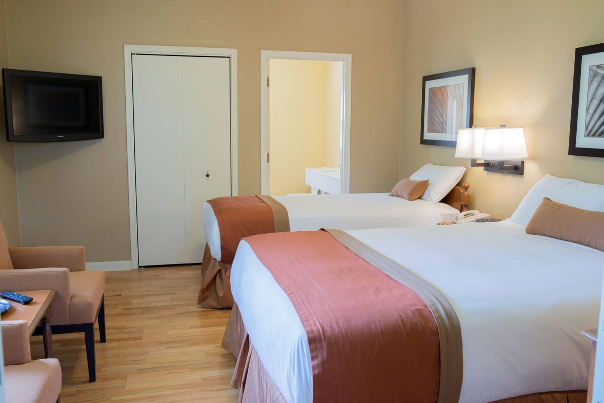 A hotel room with two beds, a TV, a desk with a chair, and a bathroom visible through an open door.