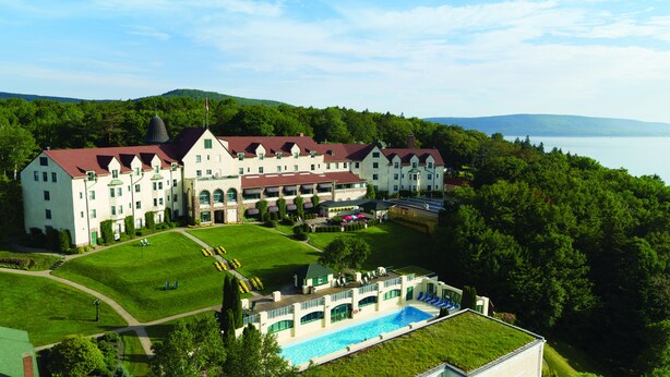 A large, multi-story hotel with a swimming pool, surrounded by lush greenery and a lake view. - Digby Pines Golf Resort and Spa (Digby)