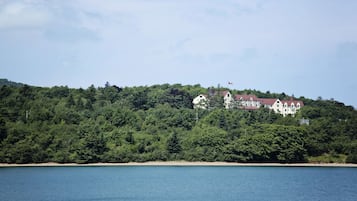 A coastal landscape with a large building on a hill, surrounded by dense greenery and a clear sky.