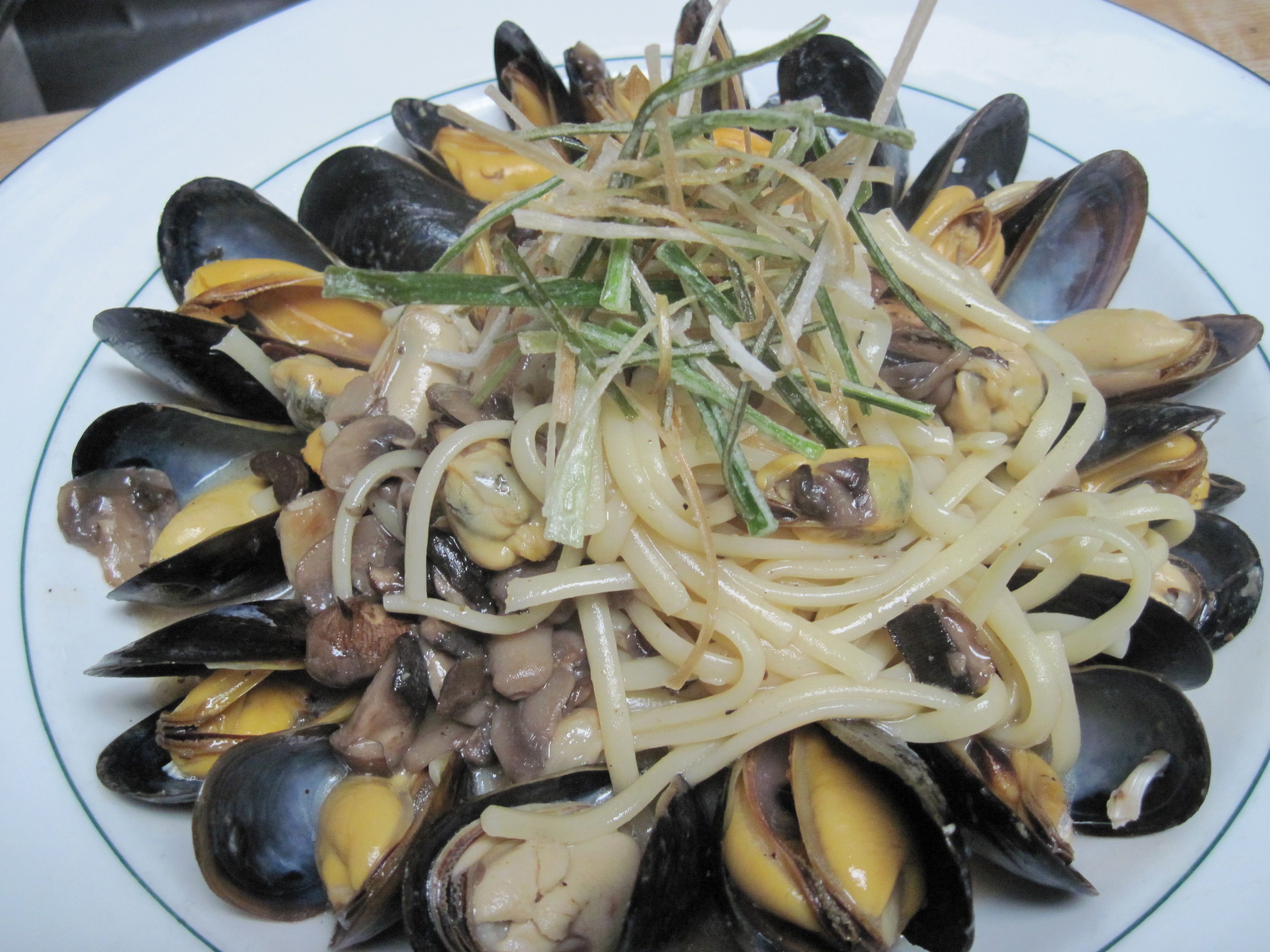 Un plato de mejillones con pasta y una guarnición de hierbas verdes.
