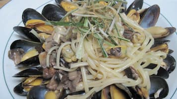 Un plato de mejillones con pasta y una guarnición de hierbas verdes.