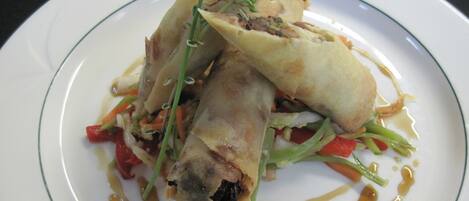 A plate of food with a rolled appetizer, vegetables, and a drizzle of sauce.