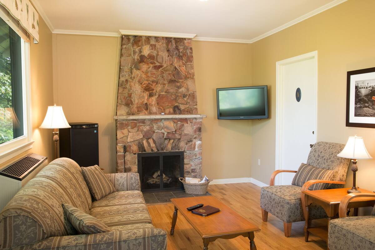 A living room with a stone fireplace, a television mounted on the wall, and a comfortable seating area with a sofa and chairs.
