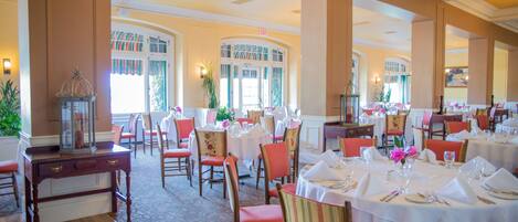A spacious dining area with multiple tables set for dining, large windows, and a chandelier.