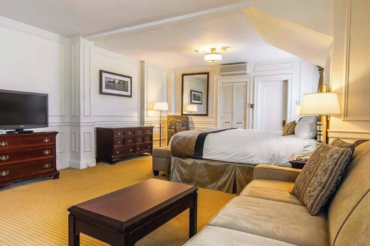 A hotel room with a bed, a sofa, a television, a dresser, and a lamp.