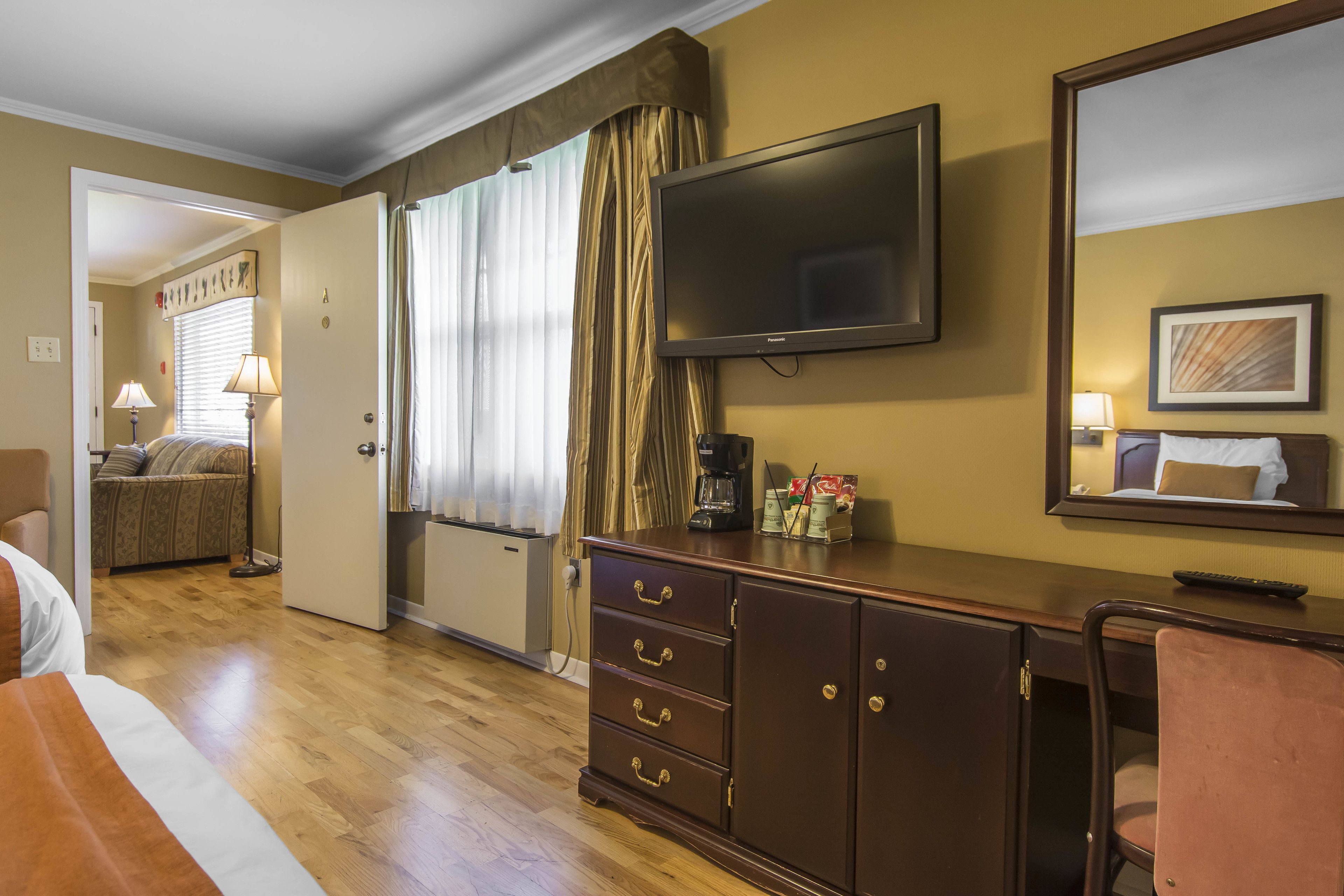 A hotel room with a bed, a desk with a TV, a dresser, a chair, and a window with curtains.