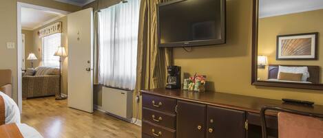 A hotel room with a bed, a desk with a TV, a dresser, a chair, and a window with curtains.