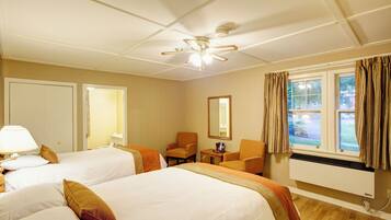 A hotel room with two beds, a chair, a small table, a ceiling fan, and a window with curtains.