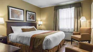 A hotel room with a large bed, two bedside lamps, a chair, and a desk.