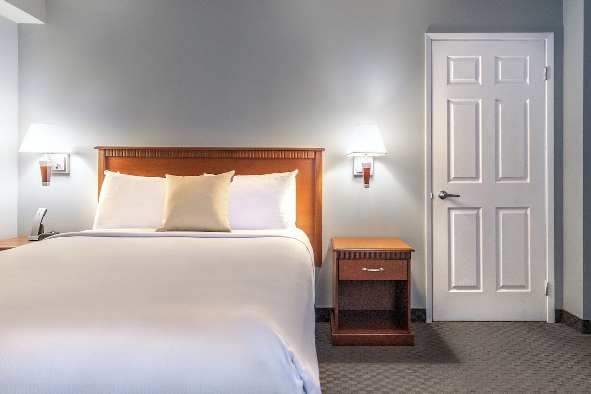 A hotel room with a large bed, two bedside lamps, a wooden nightstand, and a door.
