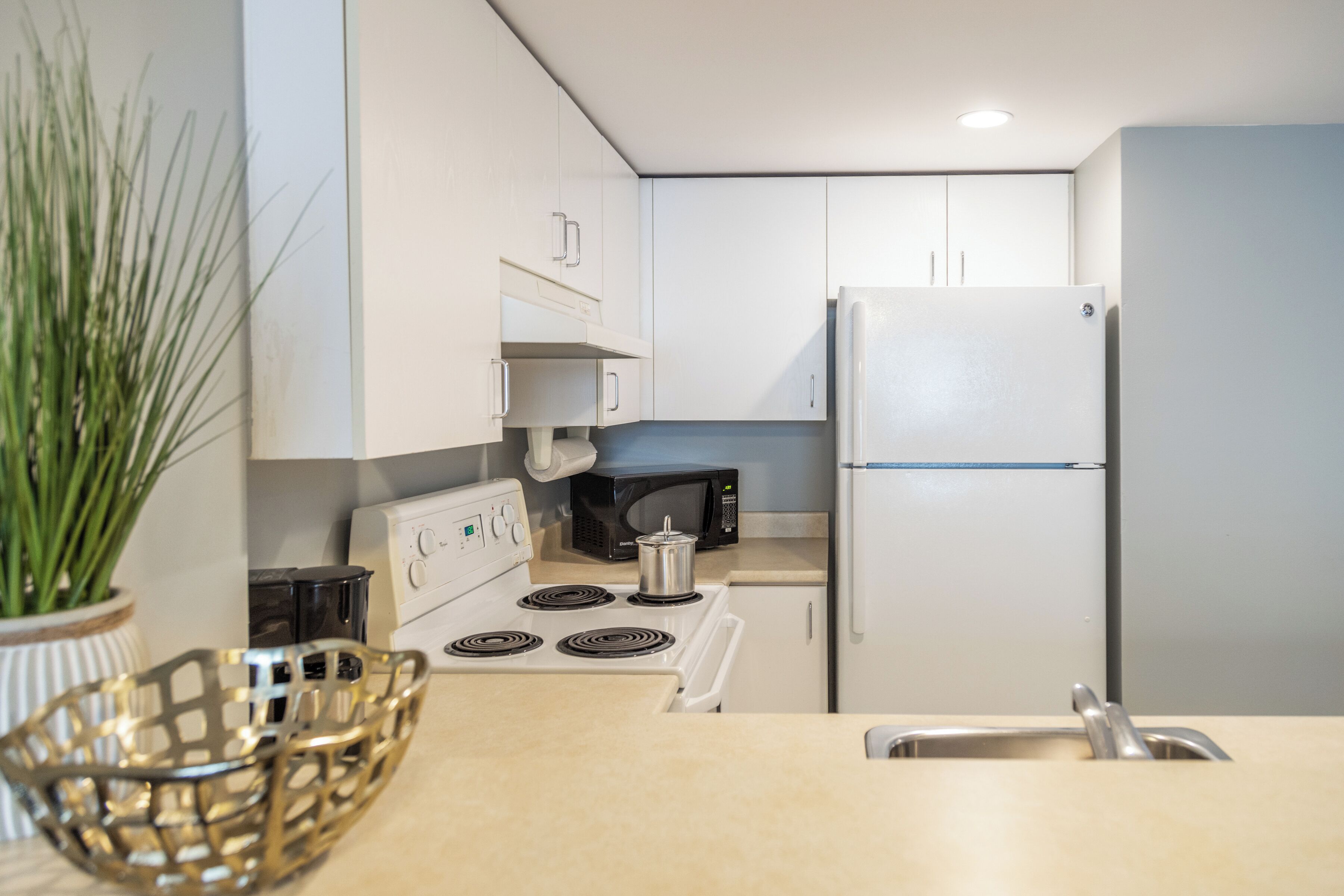Cocina compacta con gabinetes blancos, estufa, microondas y refrigerador.