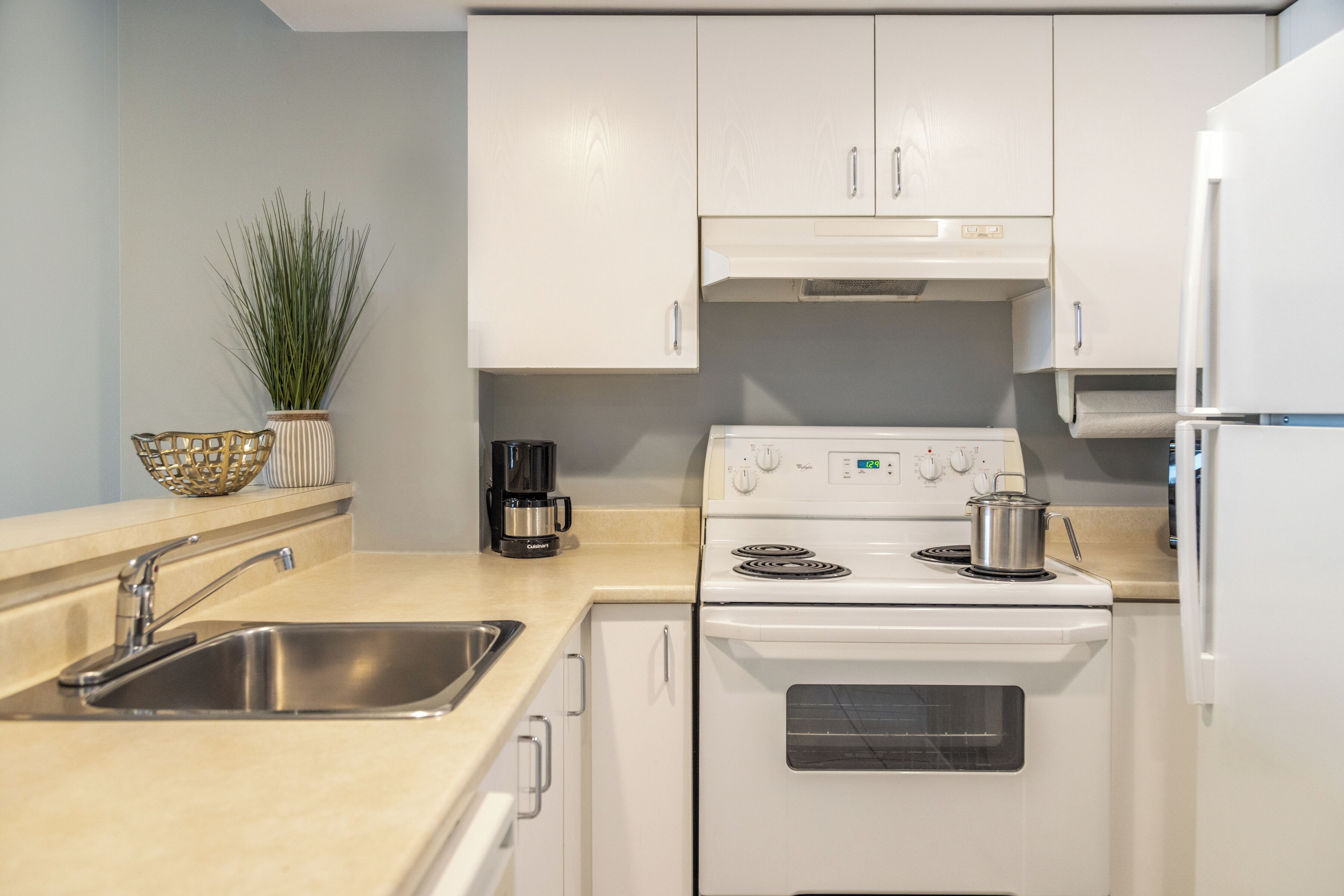 Une cuisine moderne avec des meubles blancs, un évier en acier inoxydable et une cuisinière.