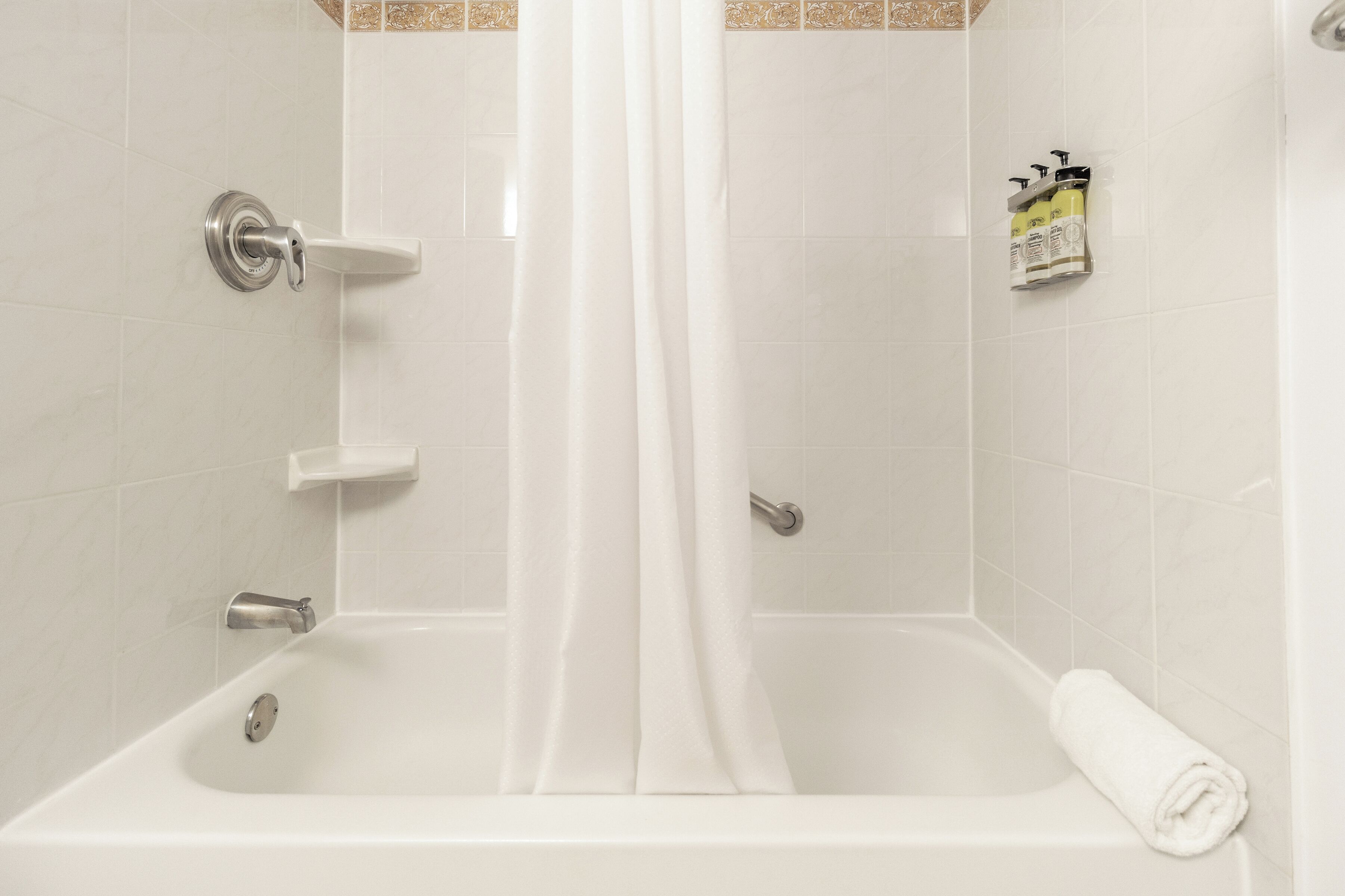 A white bathtub with a shower curtain, a towel, and a bottle of shampoo on the wall.