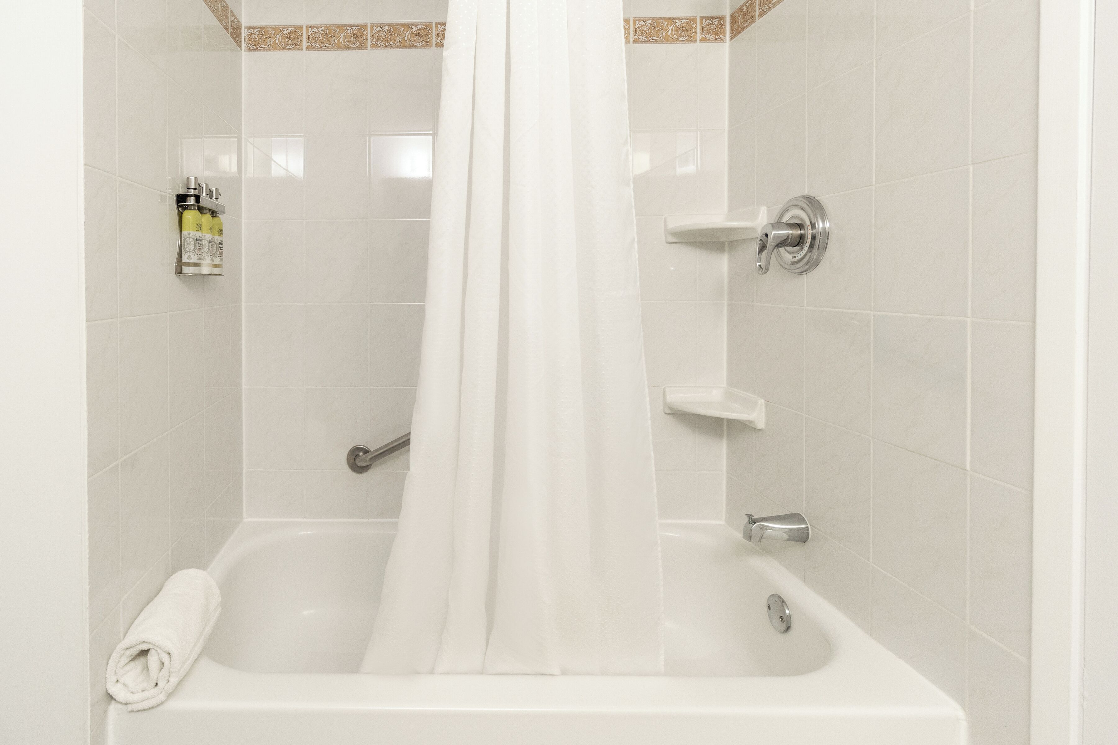 Una bañera blanca con cortina de ducha, una toalla y un dispensador de jabón.