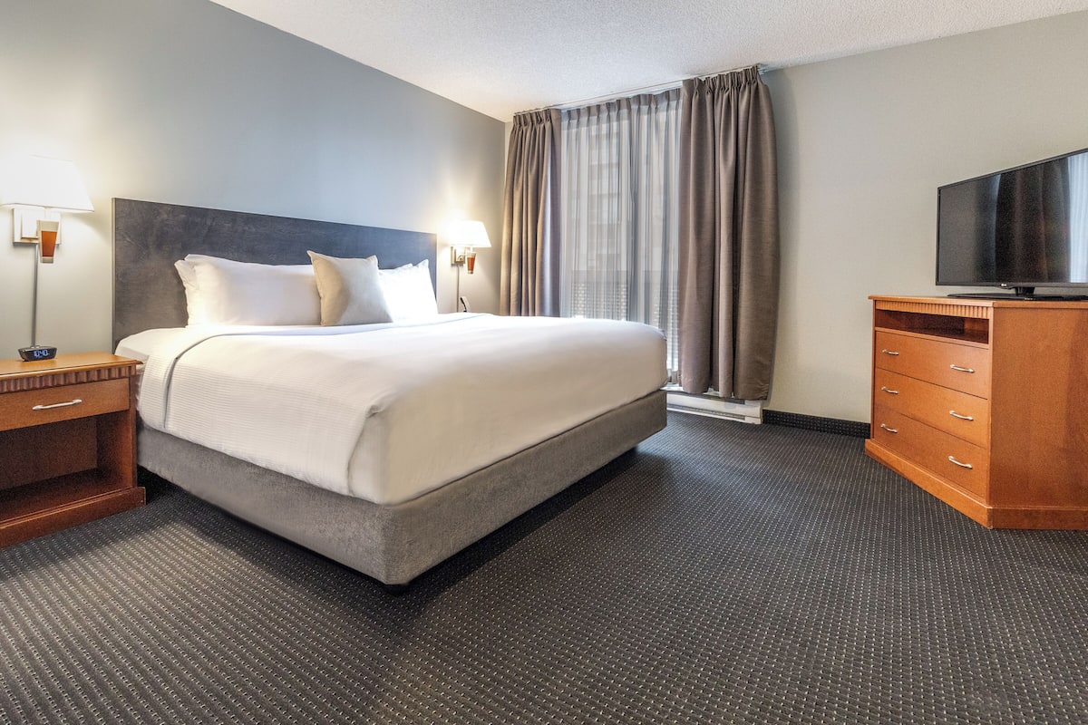 A hotel room with a large bed, a wooden dresser, a television, and a window with curtains.