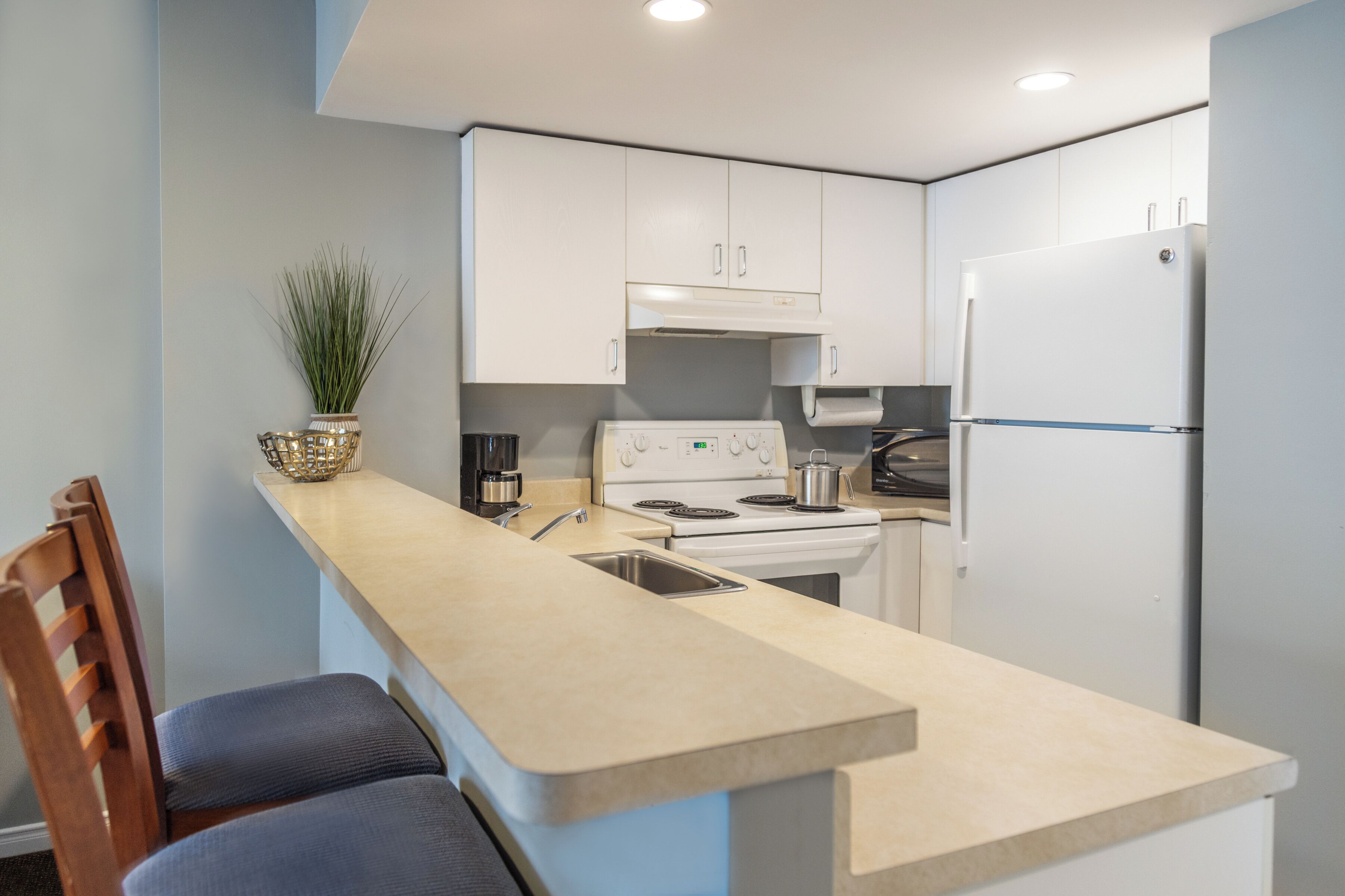 Una cocina compacta con una isla central, muebles blancos, una estufa y un refrigerador.