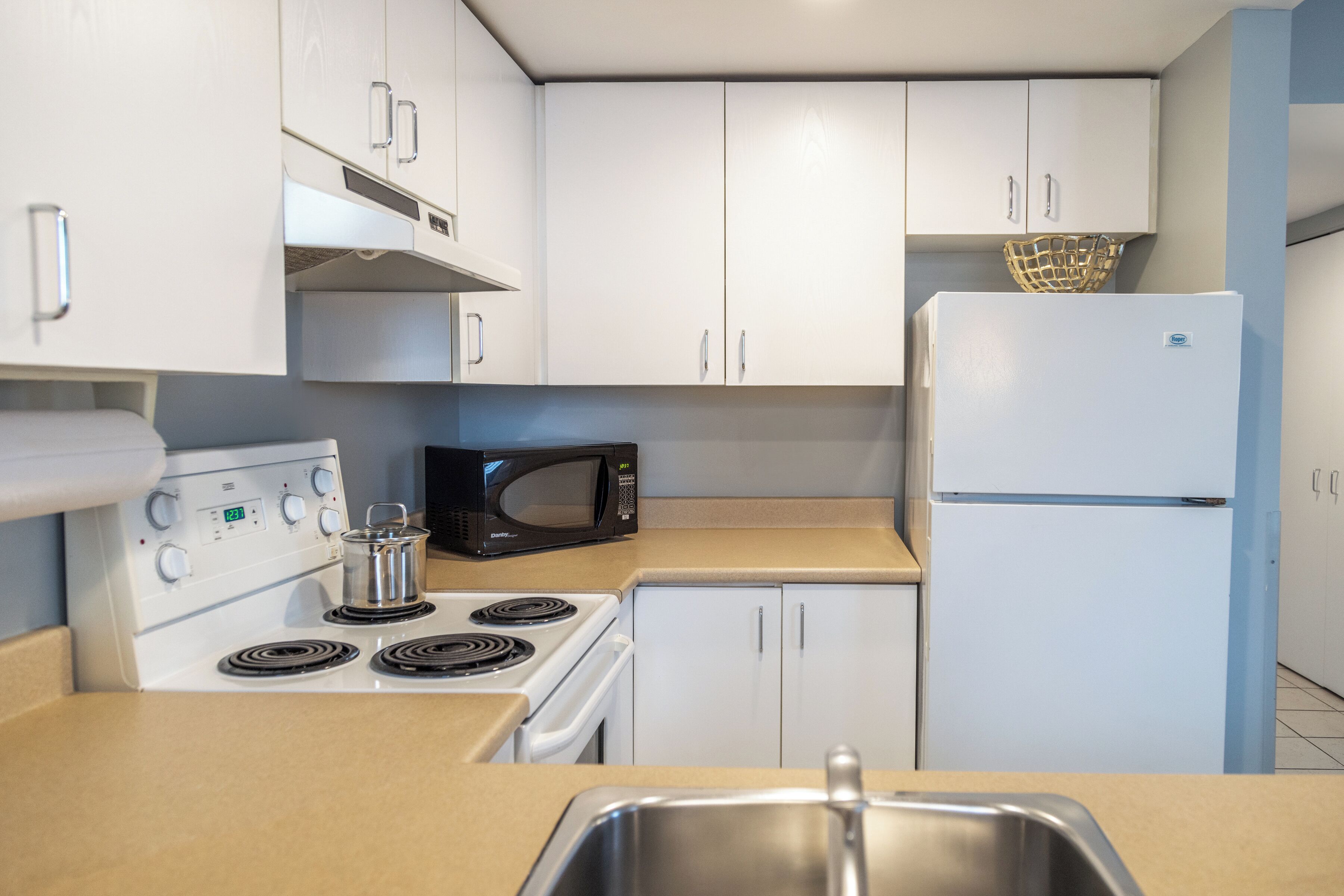 A kitchen with white cabinets, a stove, a microwave, and a refrigerator.