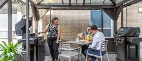 Un patio techado con pared de ladrillo, una parrilla y una mesa con sillas.