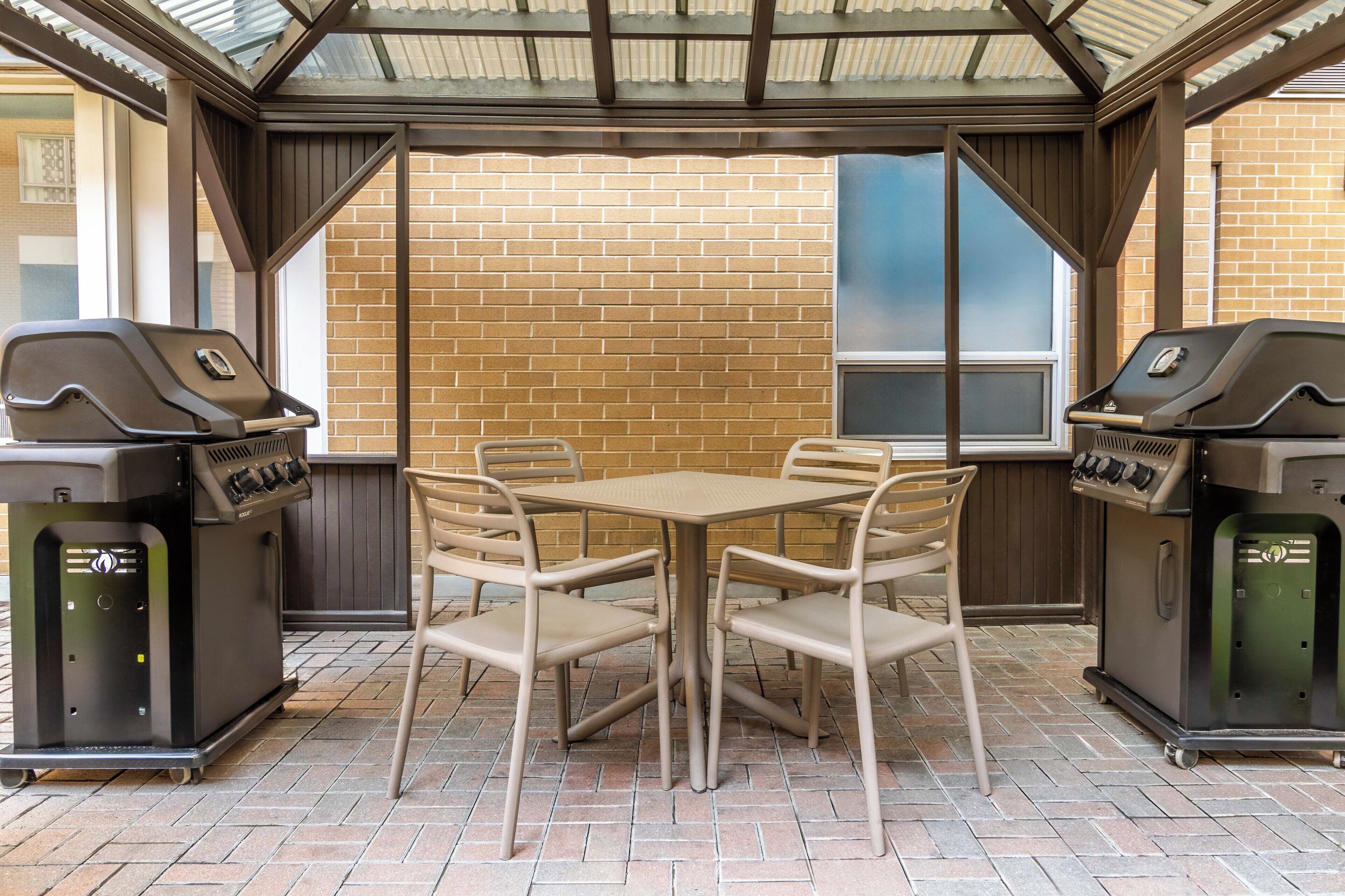 An outdoor patio with a brick floor, a table, four chairs, and two barbecue grills.