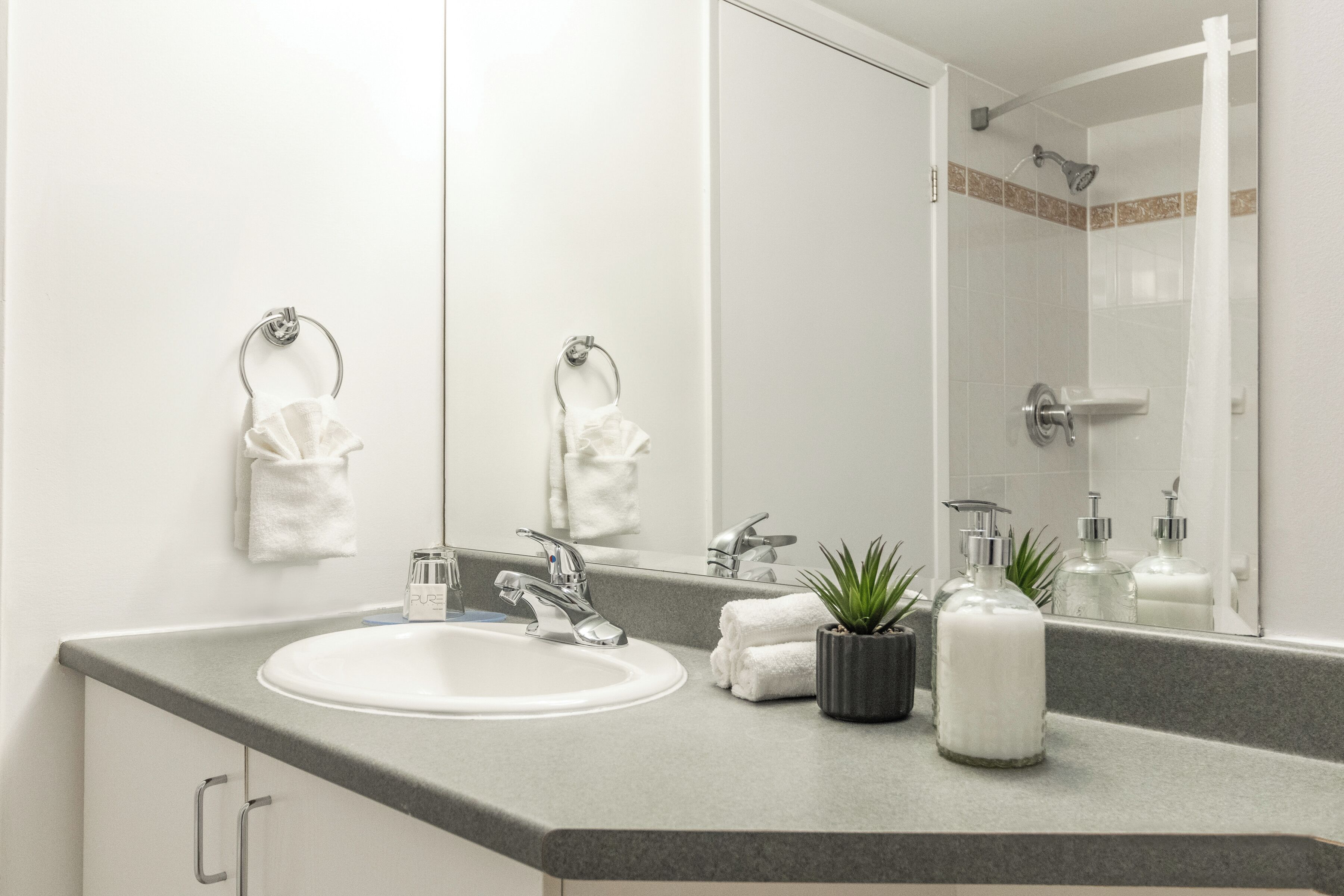 Un baño moderno con un lavamanos blanco, dos llaves, un espejo grande y una zona de ducha.