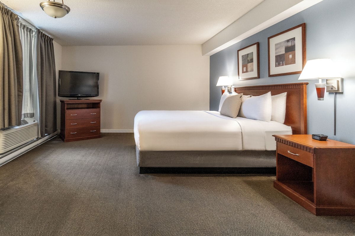A hotel room with a bed, a TV, a dresser, and a nightstand.