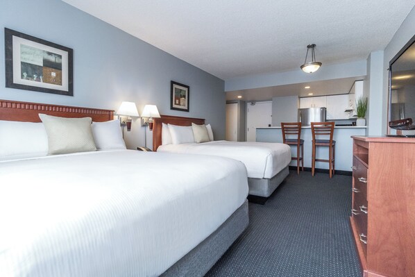 Une chambre d’hôtel avec deux lits, un bureau, des chaises, une commode et une kitchenette.