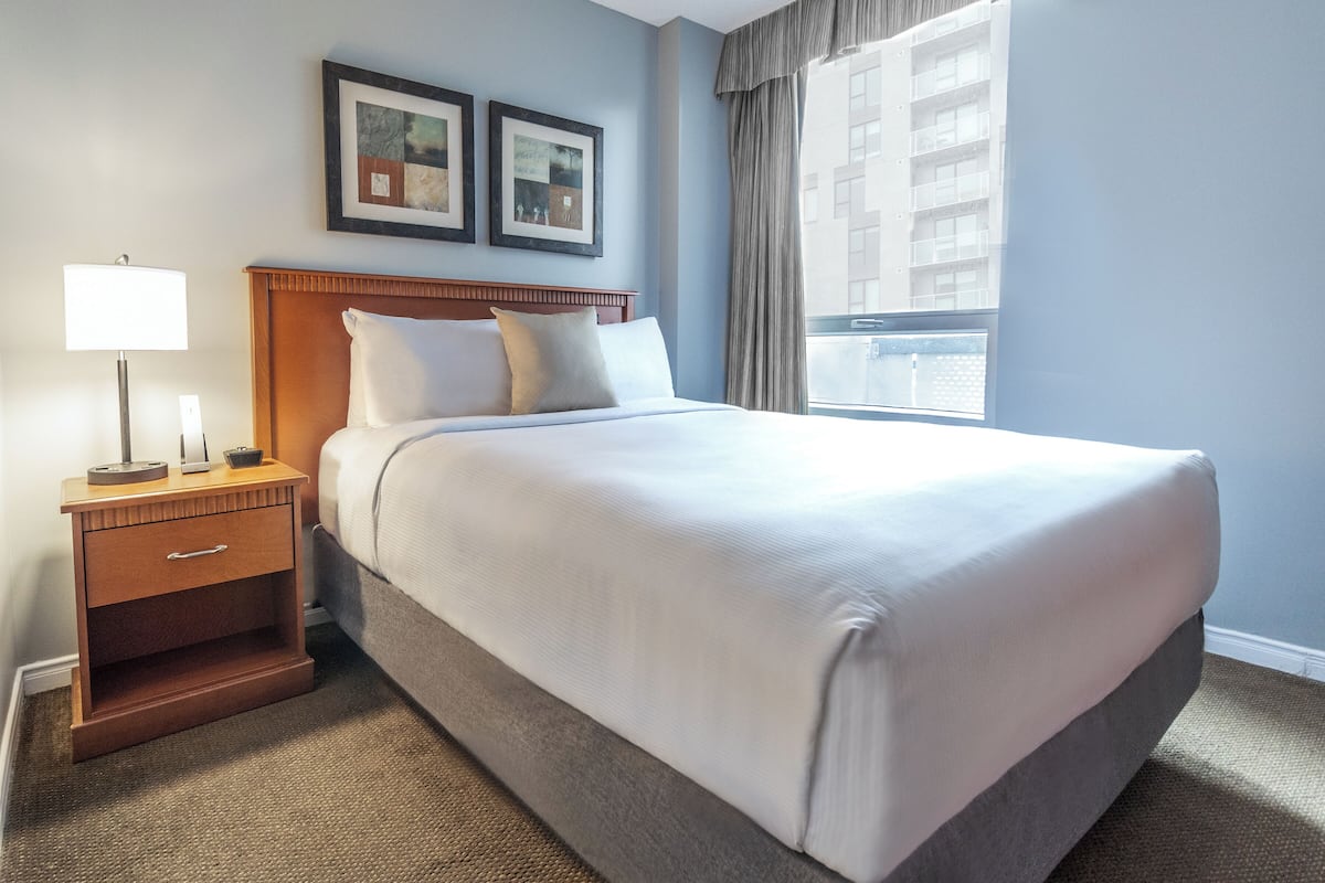 A neatly made bed with a wooden headboard, a bedside table with a lamp, and two framed pictures on the wall.