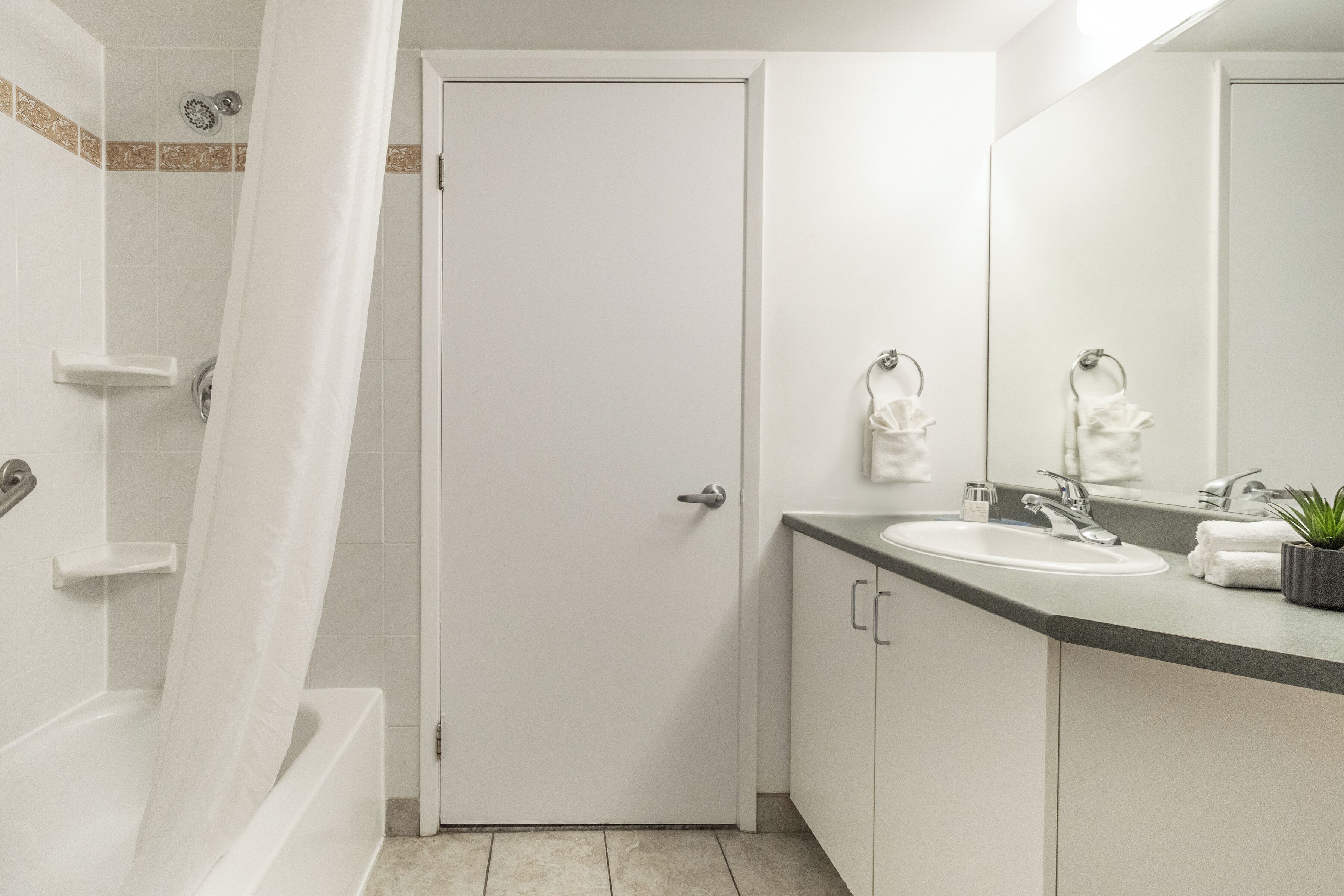 A bathroom with a bathtub, a sink, a mirror, and a door.