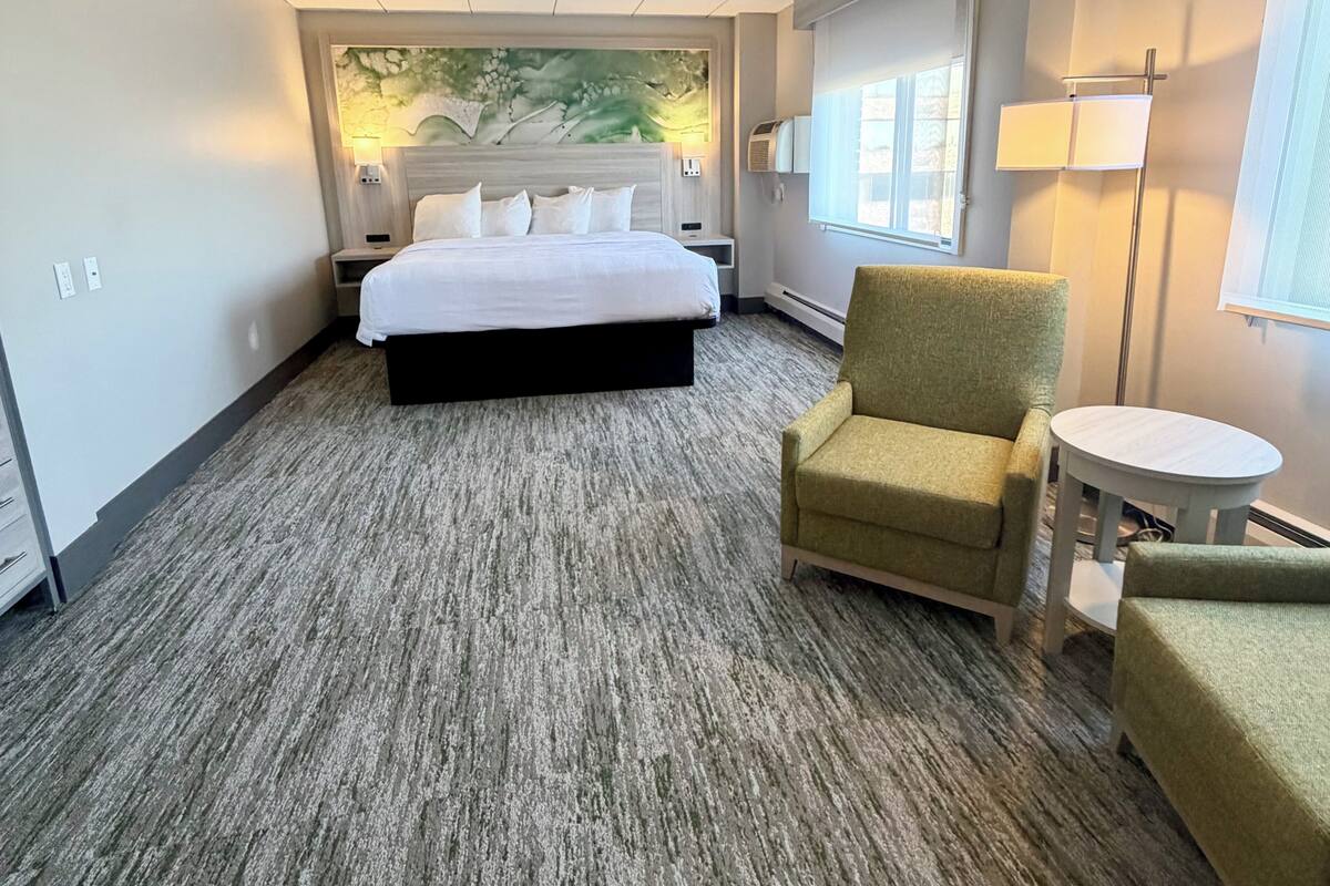 Habitación de hotel con cama, una silla, una mesita, una lámpara de pared y ventana con persianas.