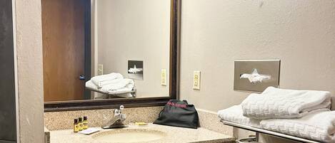 Une salle de bain équipée d’un lavabo, d’un miroir, d’un porte-serviettes et d’un tableau encadré au mur.