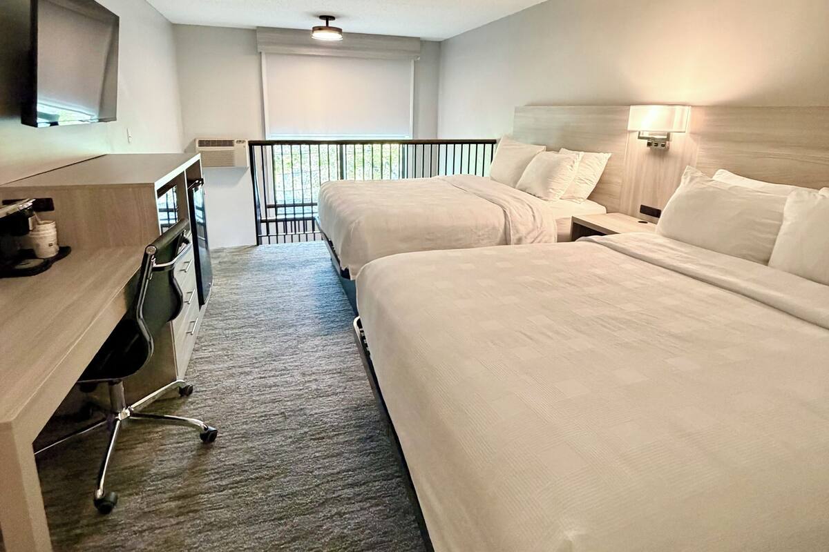 Una habitación de hotel con dos camas, un escritorio con silla, televisión y balcón.
