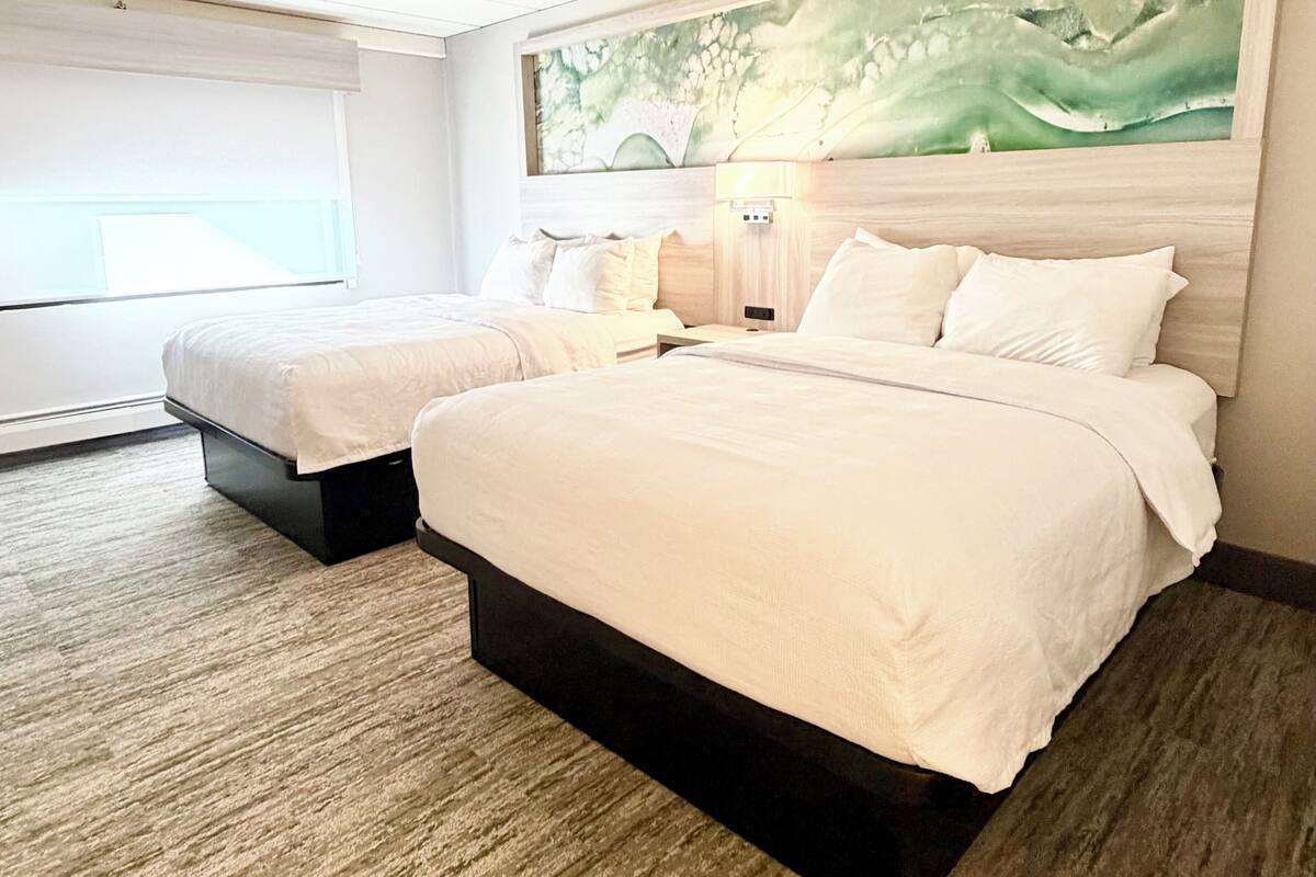 Habitación de hotel con dos camas, un cuadro grande en la pared y una ventana con persianas.