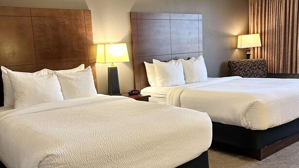 A hotel room with two beds, a nightstand, a lamp, and a clock.
