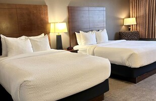 Habitación de hotel con dos camas, una mesita de noche, una lámpara y un reloj.