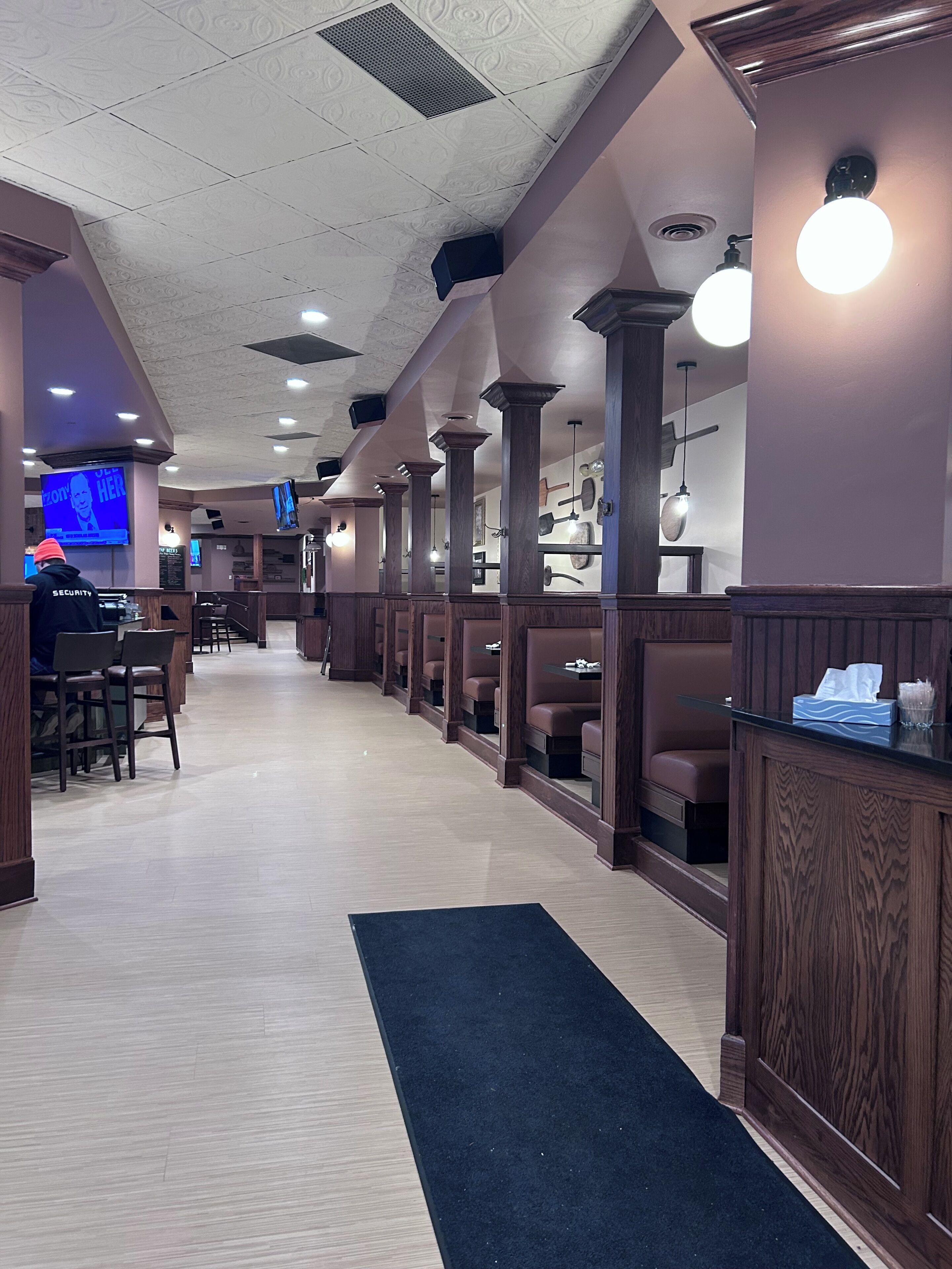 A restaurant interior with booths, wooden columns, and a black carpet leading to the counter.