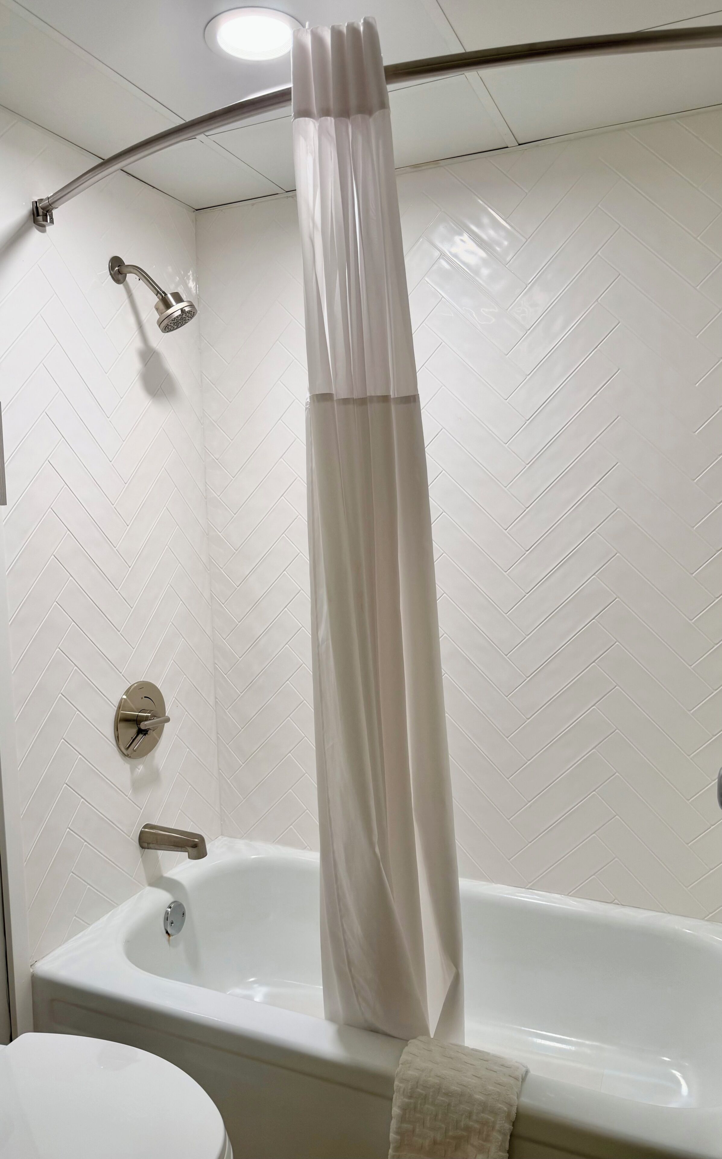 A bathroom with a white herringbone tile wall, a bathtub, a shower head, and a curtain.