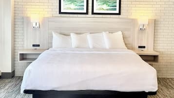 Une chambre d’hôtel avec un grand lit, deux tables de chevet fixées au mur, un mur en briques blanches et deux tableaux encadrés au-dessus du lit.