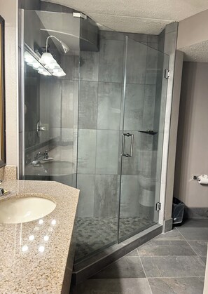 A modern bathroom with a glass-enclosed shower, a granite countertop sink, and a tiled floor. - Best Western Plus Kelly Inn (St Cloud)