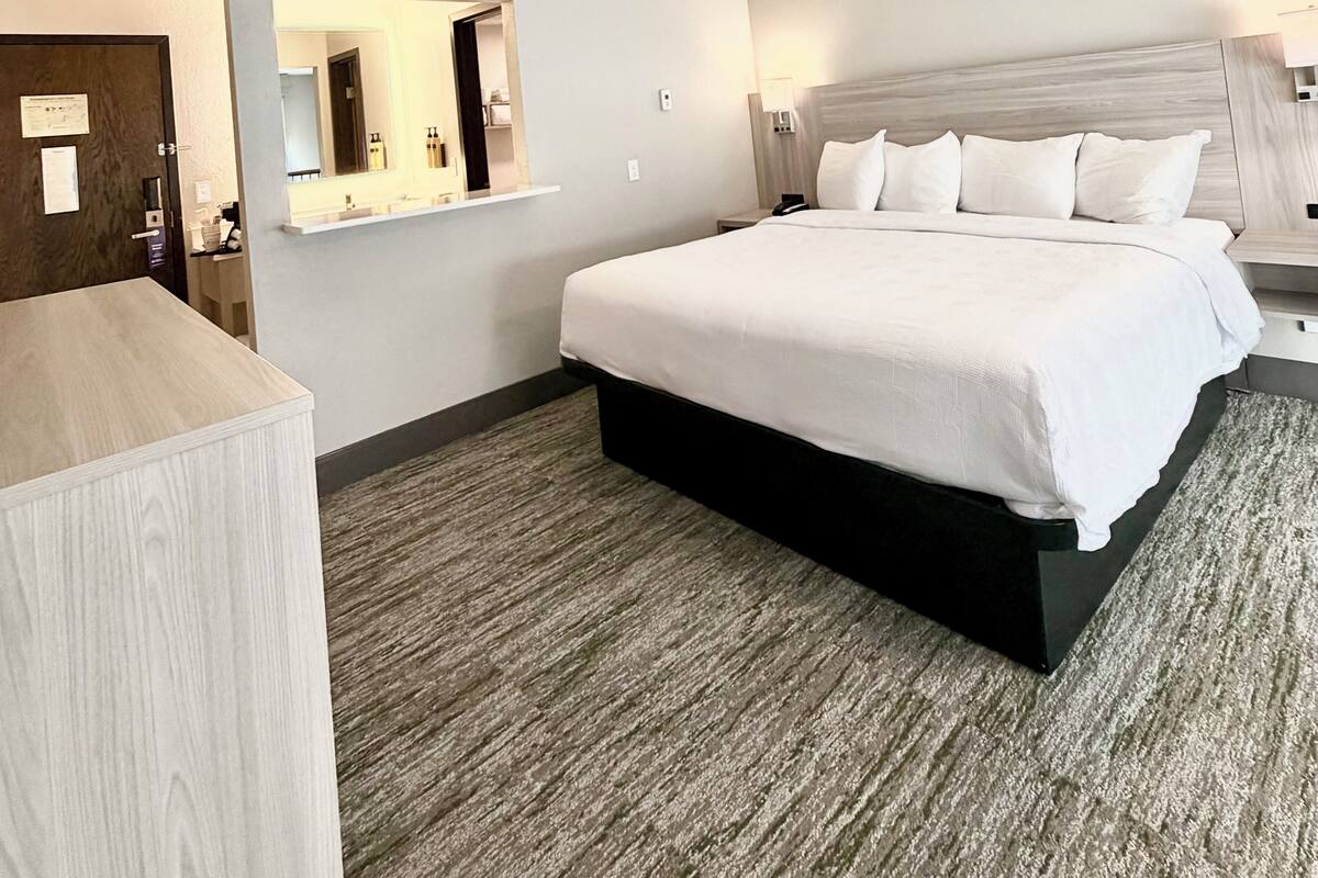 Una habitación de hotel con cama, escritorio, espejo y mesita de noche.