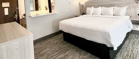 A hotel room with a bed, a desk, a mirror, and a nightstand.