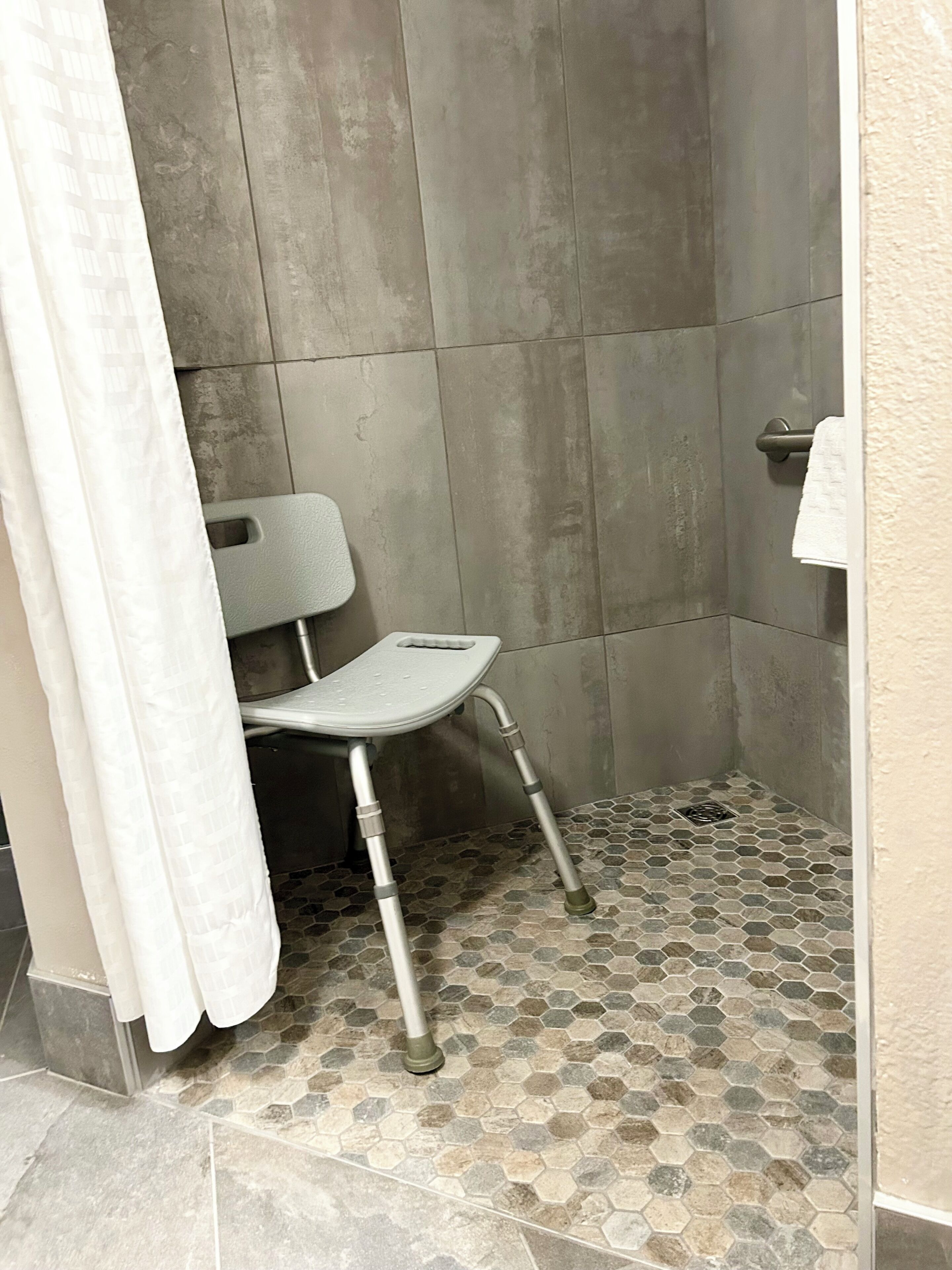 Un espace douche équipé d’un siège de douche, avec des murs et un sol carrelés.
