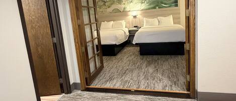 Une chambre d’hôtel avec deux lits, une porte en bois, un sol recouvert de moquette et un mur orné d’un motif abstrait vert.