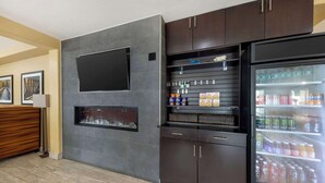A modern kitchen with dark cabinetry, a built-in TV, and a beverage refrigerator stocked with drinks. - Best Western Greentree Inn & Suites (Moore)