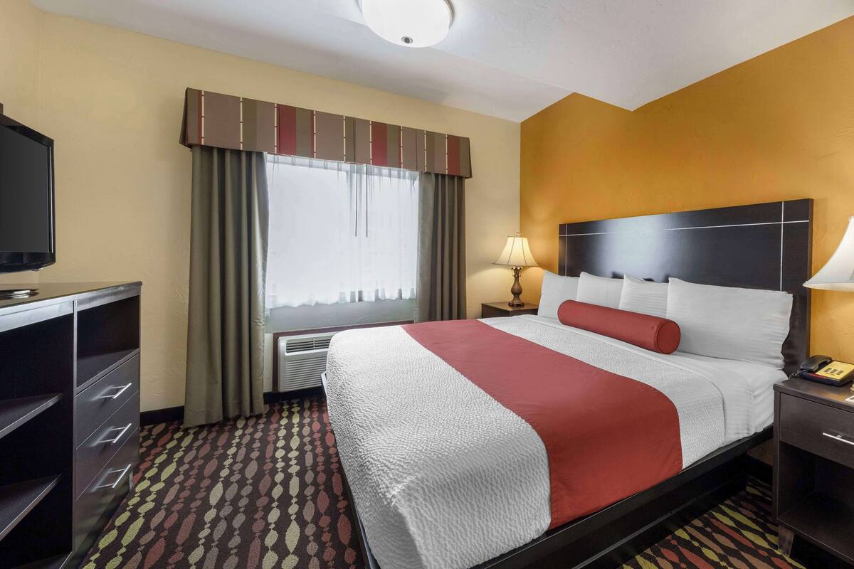 Hotellihuone, jossa on sänky, työpöytä, lamppu ja televisio.