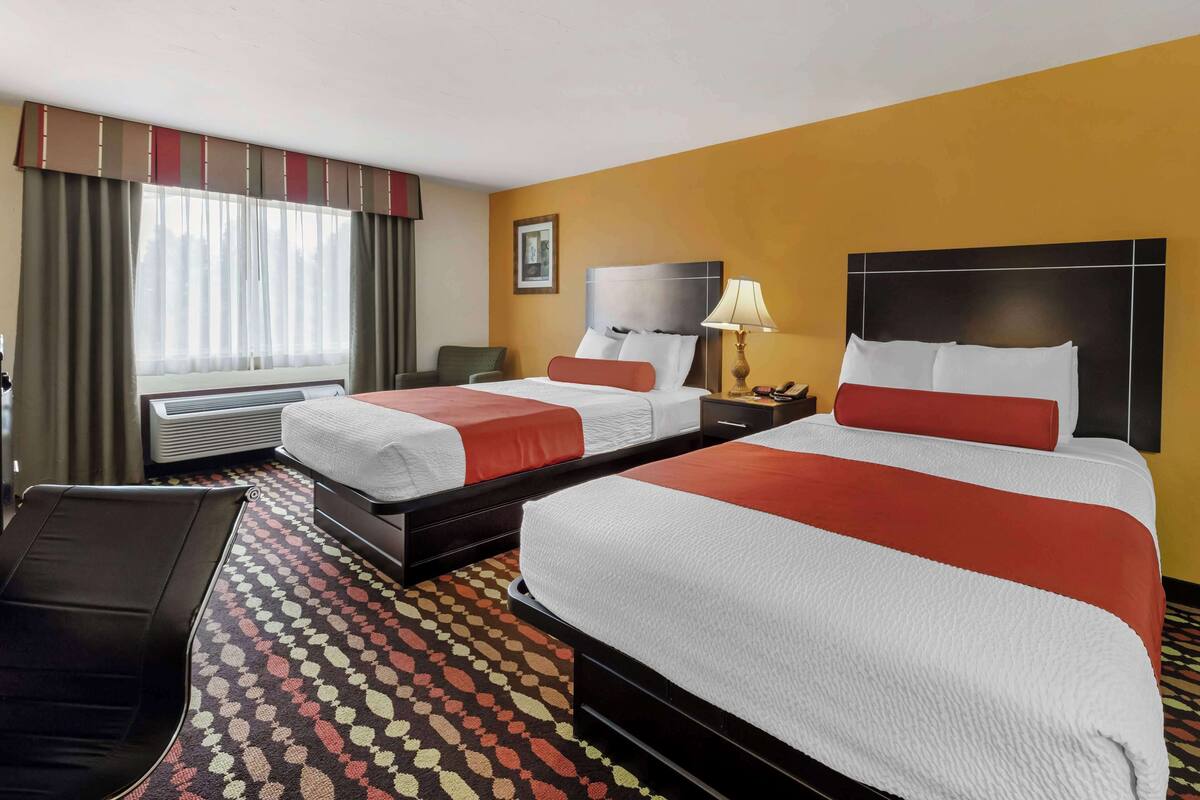 Hotellihuone, jossa on kaksi sänkyä, sohva, työpöytä ja ikkuna, jossa on verhot.