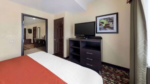 A hotel room with a bed, a television on a stand, a mirror, and a door leading to a bathroom. - Best Western Greentree Inn & Suites (Moore)